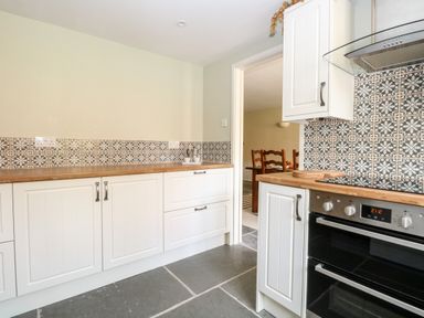 A kitchen with white cabinets wooden countertops patterned tile backsplash and a built-in oven at The Hermitage in West Beckham near Sheringham