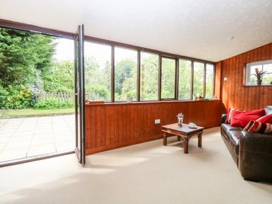 A room with wooden paneling glass windows a brown leather sofa with red cushions and a small wooden coffee table at The Hermitage in West Beckham near Sheringham