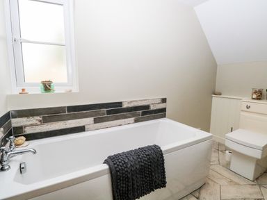 A bathroom with a bathtub towel on the edge and a toilet at The Hermitage in West Beckham near Sheringham