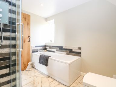 A bathroom with a bathtub a towel a glass shower wooden door and a small window at The Hermitage West Beckham near Sheringham