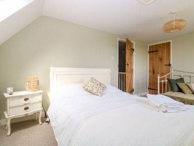 A bedroom with a white bed a nightstand with a lamp and wooden doors at The Hermitage in West Beckham near Sheringham