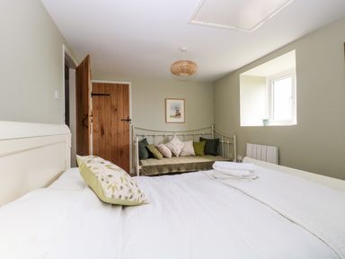 A bedroom with a bed and a daybed with cushions near a window at The Hermitage in West Beckham near Sheringham