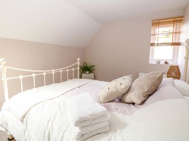 A bedroom with an iron bed frame pillows folded towels and a window with blinds at The Hermitage in West Beckham near Sheringham