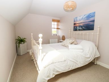 A bedroom with a metal framed bed small window painting plant and bedside table at The Hermitage in West Beckham near Sheringham
