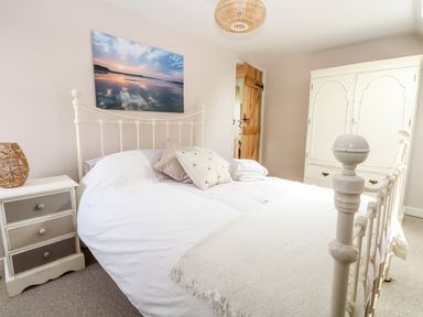 A bedroom with a white metal bed frame pillows and a side table with a wicker lamp at The Hermitage in West Beckham near Sheringham