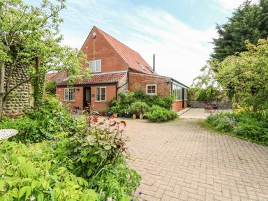 A brick house with a tiled roof and garden with plants and trees at The Hermitage in West Beckham near Sheringham