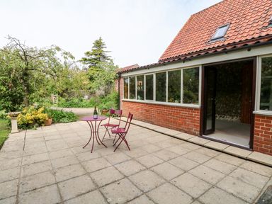 A patio with two red chairs and a red table outside a brick house with tiled roof at The Hermitage in West Beckham near Sheringham