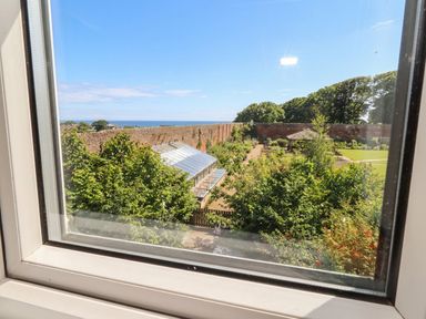 A view of a garden with a greenhouse and sea at ASTA COTTAGE in Cresswell