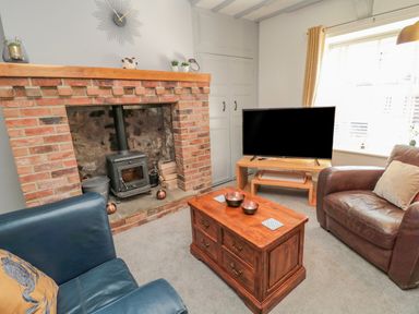 A living room with a brick fireplace a wood stove a wooden coffee table two armchairs a television on a stand and a window at Woolley Lodge in Wooler