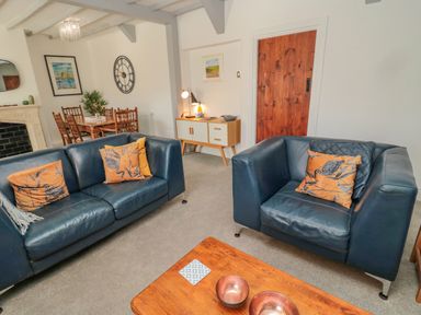 A living room with blue leather sofas and orange cushions a wooden coffee table with bowls a dining table with chairs and a wall clock and sideboard at Woolley Lodge in Wooler