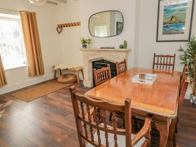 A dining room with a wooden table and six chairs a fireplace with a mirror above and a window with curtains at Woolley Lodge in Wooler