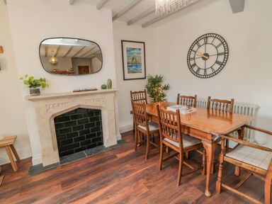 A dining room with a wooden table and six chairs a fireplace with a mirror above it and a large wall clock at Woolley Lodge in Wooler