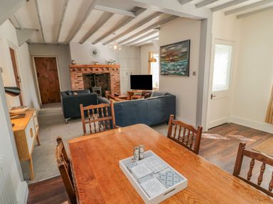 Dining area with wooden table and chairs opening into a living room with blue sofas and brick fireplace at Woolley Lodge in Wooler