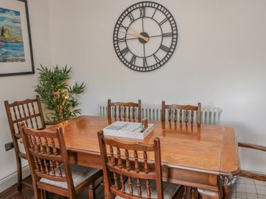 A dining room with a wooden table and six wooden chairs a large wall clock and a framed picture at Woolley Lodge in Wooler