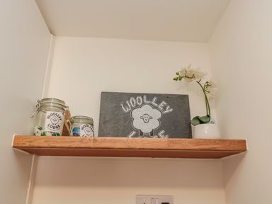 A wooden shelf with two jars, a sign that says Woolley Lodge, and a white vase with white flowers at Woolley Lodge in Wooler
