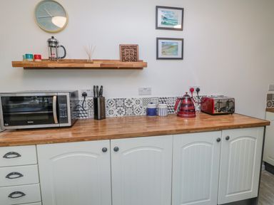 A kitchen counter with microwave knives kettle toaster and cups with a wall clock and framed pictures above at Woolley Lodge in Wooler