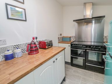 A kitchen with wooden countertops a black oven a red toaster and kettle and blue and white canisters at Woolley Lodge in Wooler