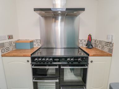 A kitchen with a black stove and oven between white cabinets and wooden countertops at Woolley Lodge in Wooler