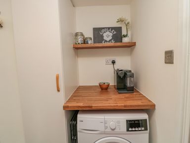 A laundry area with a washing machine a wooden countertop a coffee machine a bowl a shelf with jars and a plant at Woolley Lodge in Wooler