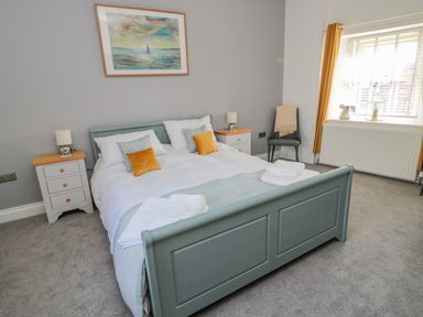 A bedroom with a double bed two bedside tables lamps a chair and a window with curtains at Woolley Lodge in Wooler