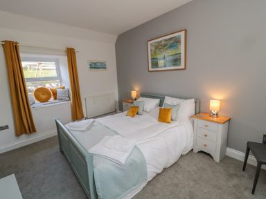 A bedroom with a double bed two bedside tables with lamps and a window seat with cushions at Woolley Lodge in Wooler