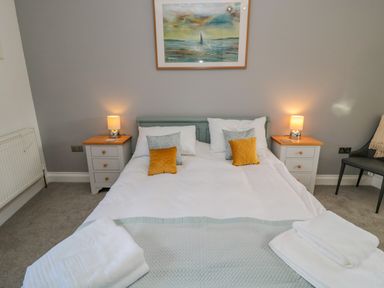 A bedroom with a double bed two bedside tables with lamps a framed painting and a chair with a blanket at Woolley Lodge in Wooler