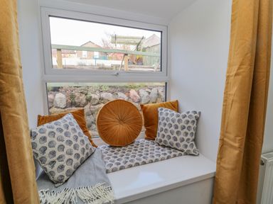A window seat with cushions and a blanket by a window with curtains at Woolley Lodge in Wooler