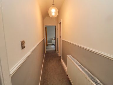 A narrow hallway with beige carpet and two-tone walls featuring a radiator along one side at Woolley Lodge in Wooler