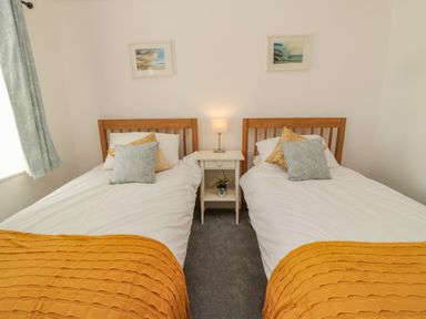 A bedroom with two single beds a bedside table with a lamp and framed pictures on the wall at Woolley Lodge in Wooler