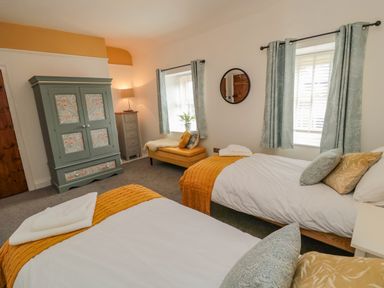A bedroom with two single beds yellow bed runners pillows a green wardrobe a yellow bench and blue curtains at Woolley Lodge in Wooler