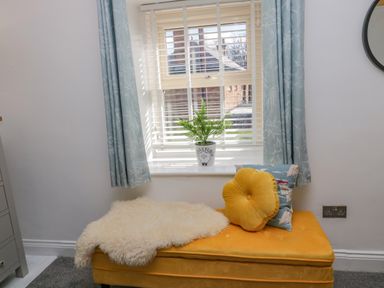 A window with blue curtains and white blinds above a yellow bench with two cushions and a plant on the windowsill at Woolley Lodge in Wooler