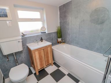 A bathroom with a toilet sink vanity and bathtub with grey wall tiles and checkered floor at Woolley Lodge in Wooler