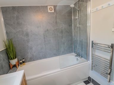 A bathroom with a bathtub shower combination a glass shower screen a towel rack a potted plant and toiletries at Woolley Lodge in Wooler
