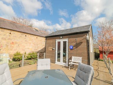 A wooden lodge with glass doors and outdoor seating on a wooden deck at Woolley Lodge in Wooler
