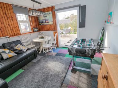 A game room with a foosball table a small round table with chairs a black sofa and a door leading outside at Woolley Lodge in Wooler