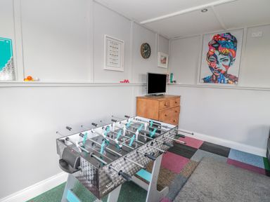 A room with a foosball table a wooden chest of drawers with a TV on top a clock and framed pictures on the wall at Woolley Lodge in Wooler