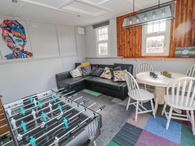 A game room with a foosball table black sectional sofa a round table with four white chairs and two windows at Woolley Lodge in Wooler