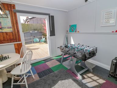 A game room with a foosball table a chess table and chairs and sliding glass doors opening to an outdoor deck at Woolley Lodge in Wooler