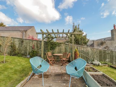 A backyard with two blue chairs a wooden pergola table and chairs and raised garden beds at Woolley Lodge in Wooler