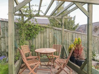 A wooden pergola with a round table and four chairs next to a wooden fence in a garden at Woolley Lodge in Wooler