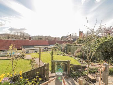 A garden with grass lawn wooden gate paved pathway and flowers at Woolley Lodge in Wooler