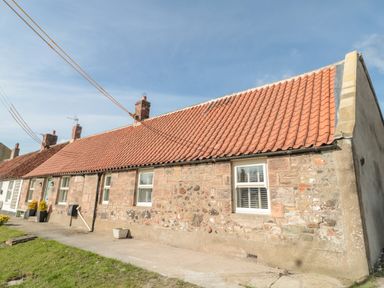 A row of stone cottages with tiled roofs and chimneys under a blue sky at Woolley Lodge in Wooler