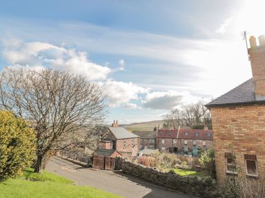 A street view with brick houses trees and hills in the background at Woolley Lodge in Wooler