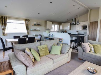 A living room with sofas and cushions next to a dining table with chairs and a kitchen with bar stools at The Potting Shed in New Quay