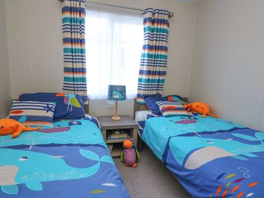 A bedroom with two single beds with ocean-themed bedding and striped curtains at The Potting Shed in New Quay
