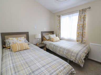 A bedroom with two single beds a nightstand with a lamp and a window with curtains at The Potting Shed in New Quay