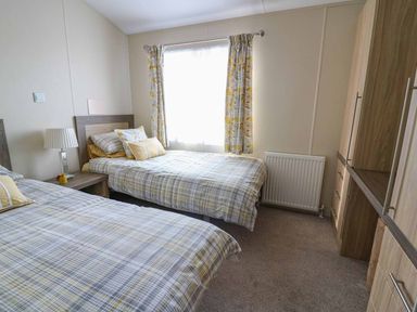 A bedroom with two single beds a nightstand with a lamp and wardrobe with drawers at The Potting Shed in New Quay