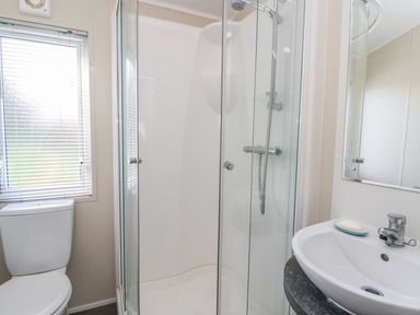 A bathroom with a shower enclosure sink with a soap dish and a toilet near a window at The Potting Shed in New Quay