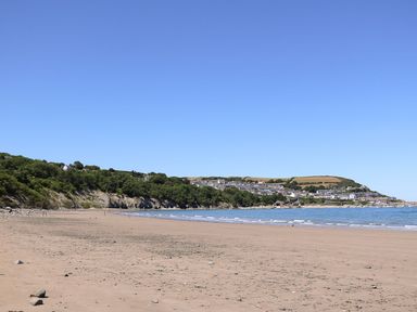A sandy beach with a coastline and houses on hills under a clear blue sky at The Potting Shed in New Quay
