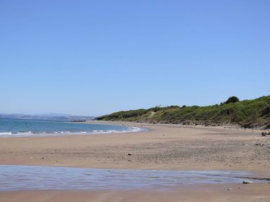 A wide sandy beach with small waves and greenery on cliffs at The Potting Shed in New Quay